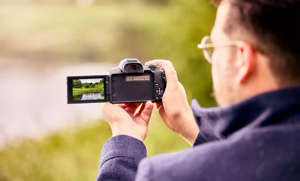 Чоловік знімає пейзаж на Canon EOS R50, поворотний екран відкинуто вбік, у кадрі видно параметри витримки 1/125 і діафрагми f/6.3