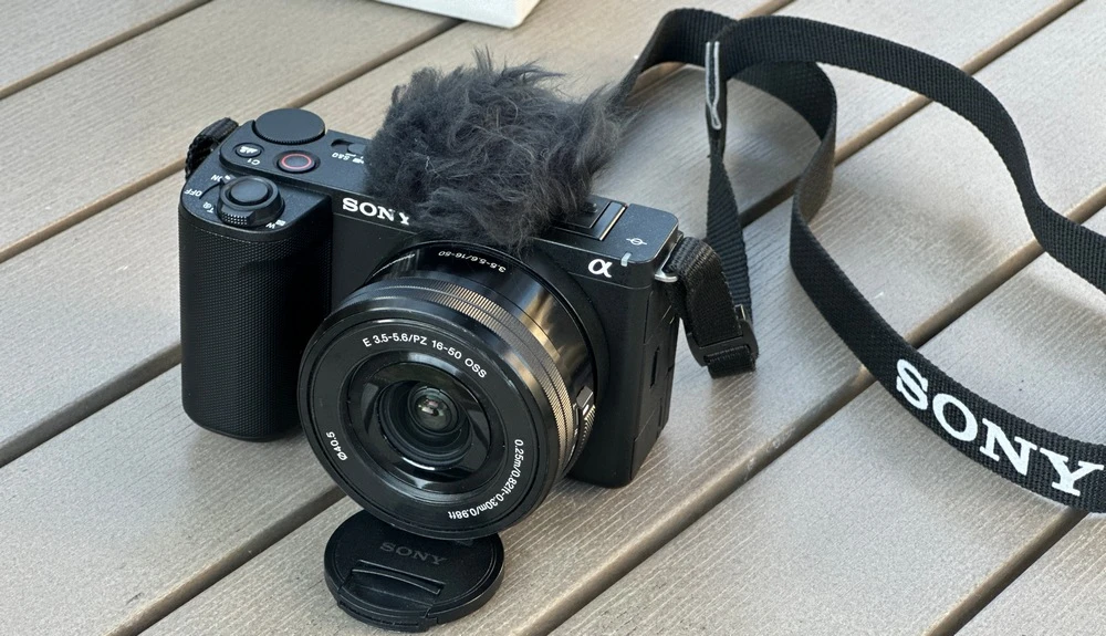 Sony ZV-E10 II із китовим об'єктивом E PZ 16-50mm f/3.5-5.6 OSS і хутряним вітрозахистом на мікрофоні лежить на дерев'яному столі